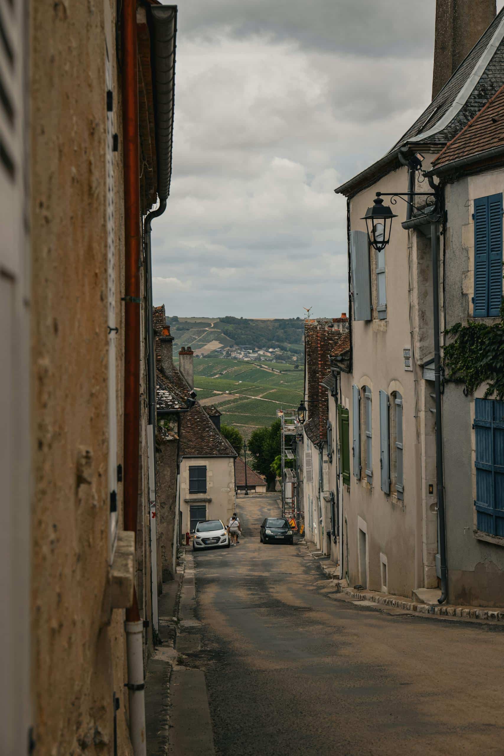 Explore a quaint street in Sancerre, France, with classic architecture and a scenic vineyard view.